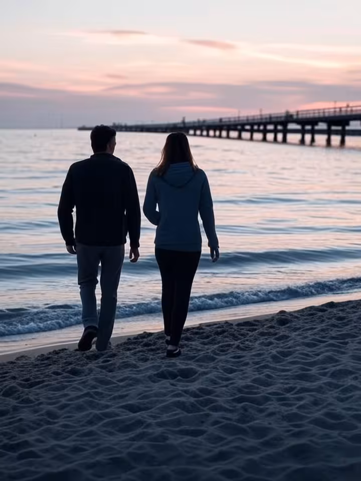 Romantic beach walk on Sopot sandy shore at dusk, silhouettes of couple, wooden pier extending into